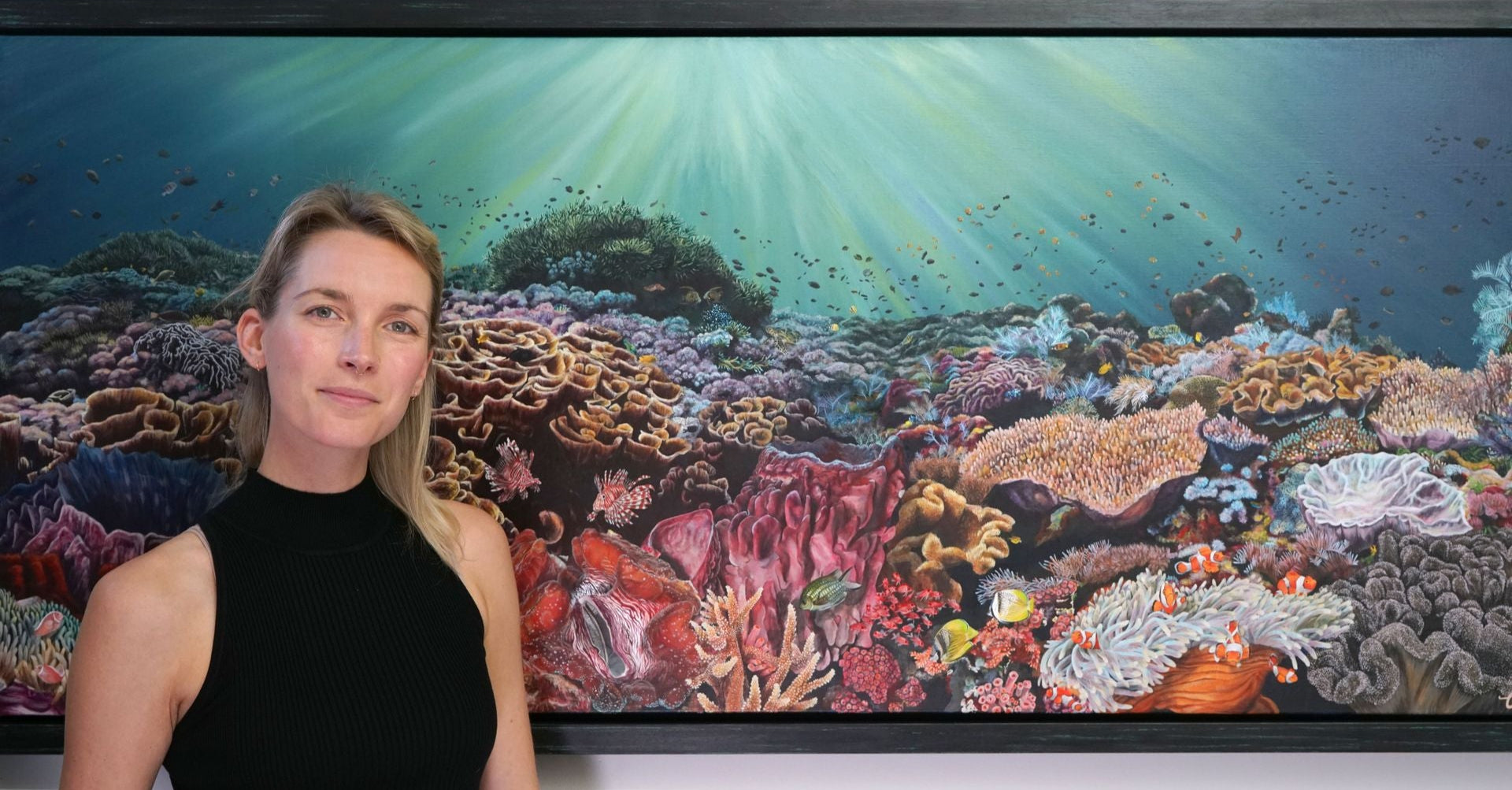 charlotte sutton wildlife artists in london next to large painting of underwater ocean scene with fish